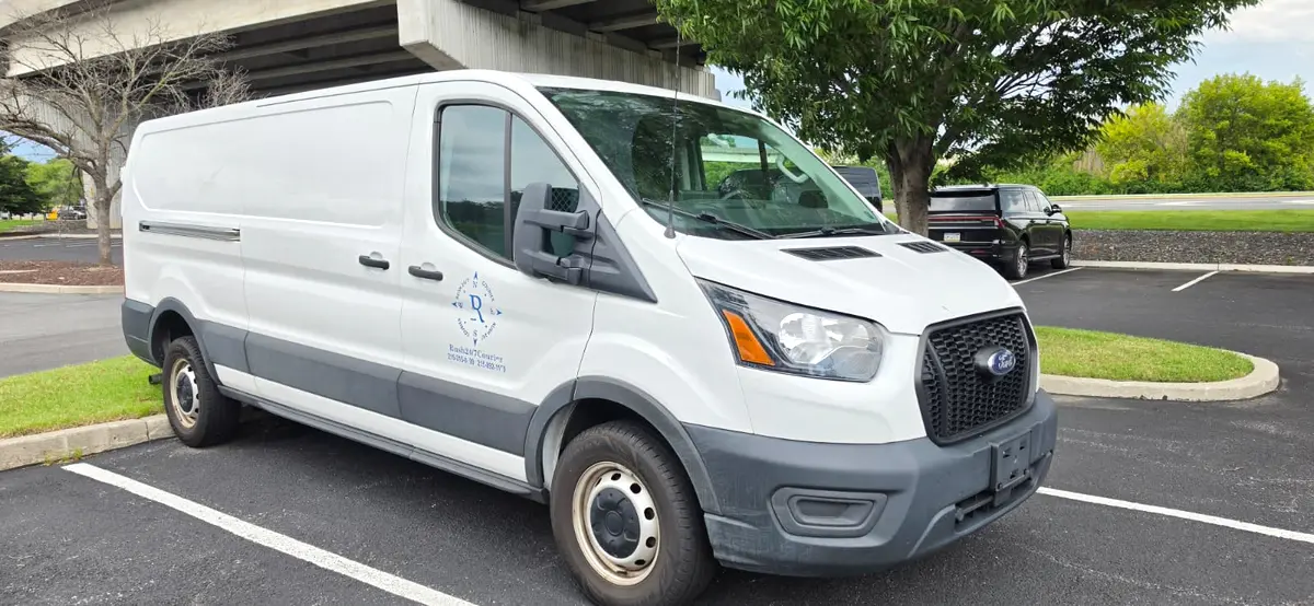 White Rush 24/7 Ford Transit cargo van, front three-quarter view, with the blue compass logo and dispatch phone numbers on the door